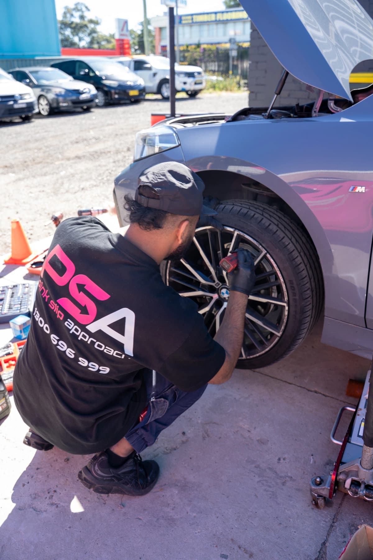 A Pink Slip Approach technician checking a wheel on a grey BMW, tools laid out beside him